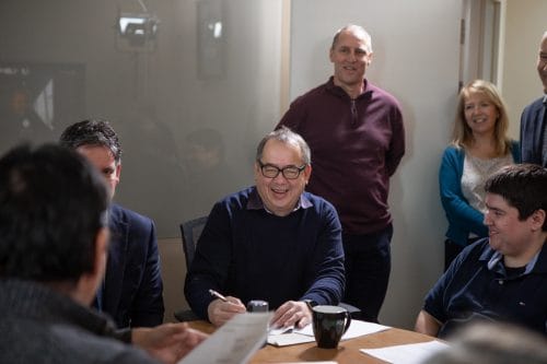 PQA CEO Keith McIntosh Sitting Around Table with Employees Laughing